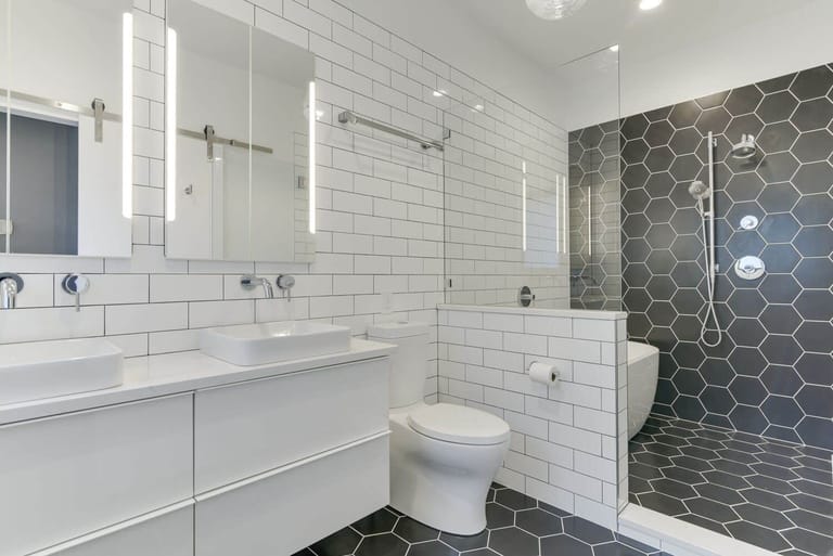 Floating vanity with dual sinks and wall-mounted fixtures, featuring subway tile walls and hexagon tile flooring.